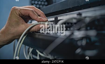 Maintenance of LAN or web servers. Close up of system administrator connecting cables with server rack, working in server room. Operation of information systems and networks. Data storage center. Stock Photo