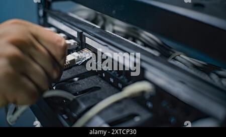 Male network administrator inserts cables into the server rack working with internet equipment in server room. Maintenance of LAN, computer networks and web servers. Data storage center. Close Up. Stock Photo