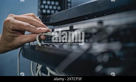 Maintenance of LAN or web servers. Close up of system administrator connecting cables with server rack, working in server room. Operation of information systems and networks. Data storage center. Stock Photo