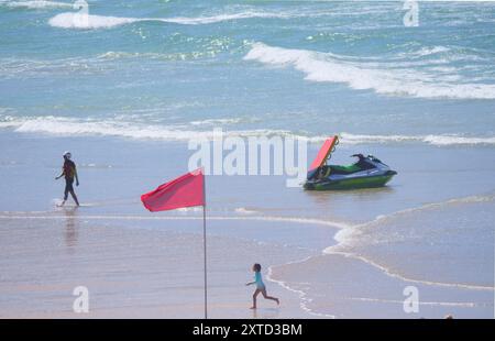 A Red Flag beach safety shutdown for thousands of visitors. RNLI Lifeguards take an unpopular but necessary action by advising swimmers and surfers to vacate the water. Although the popular beach famous for being the home of British surfing is thronged from end to end with record crowd numbers, a decision in light of big, rough, wave conditions combined with an outgoing tide resulted in the Red flags being hoisted to avoid folk getting into difficulties.  A number of major beach safety rescues have taken place in the resort in previous days, including 200 people being evacuated from Whipsiderr Stock Photo