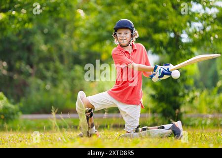 Kids playing cricket in summer park. Boy with bat and ball on cricket pitch. Helmet and guard for safe game. Sport for active child. Stock Photo