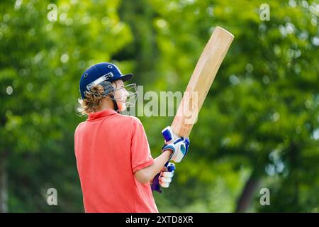 Kids playing cricket in summer park. Boy with bat and ball on cricket pitch. Helmet and guard for safe game. Sport for active child. Stock Photo