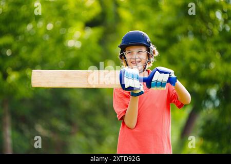 Kids playing cricket in summer park. Boy with bat and ball on cricket pitch. Helmet and guard for safe game. Sport for active child. Stock Photo