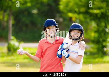 Kids playing cricket in summer park. Boy with bat and ball on cricket pitch. Helmet and guard for safe game. Sport for active child. Stock Photo