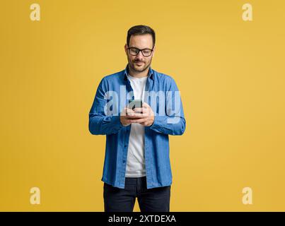 Confident serious businessman checking messages over mobile phone isolated on yellow background Stock Photo