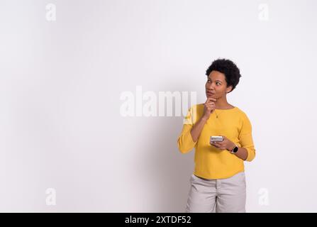 Thoughtful female entrepreneur with smartphone touching chin and looking away on white background Stock Photo