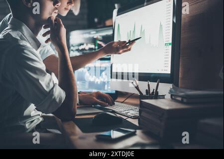 Analyzing data. Close-up of young business team working together in creative office while young woman pointing on the data presented in the chart with Stock Photo