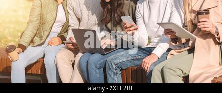 Cropped of international friends using diverse gadgets in park Stock Photo