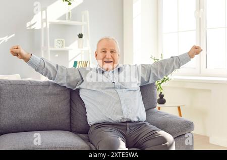 Portrait of a gray-haired elderly excited senior man sitting on sofa in the living room at home Stock Photo