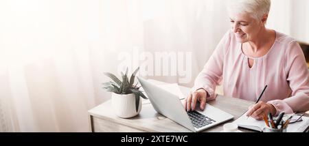 Top view of mature working lady making notes, using laptop Stock Photo