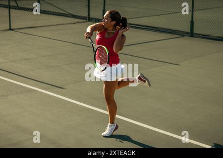 Competitive female tennis player in action hitting a powerful forehand shot during a game on an outdoor court Stock Photo