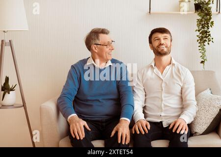 Cheerful Adult Son And Senior Father Talking Sitting On Sofa At Home Stock Photo