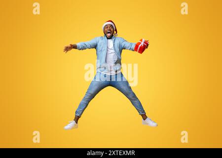 Overjoyed afro guy in santa hat jumping with gift box Stock Photo