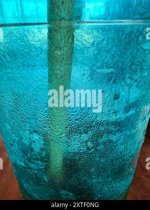 Closeup shows ice crystals forming on a colorful drink glass with a paper straw at restaurant. Stock Photo