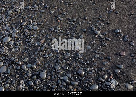 Black volcanic sand beach with shiny volcanic stones background on Reynisfjara Black Sand Beach, Iceland, top view. Stock Photo