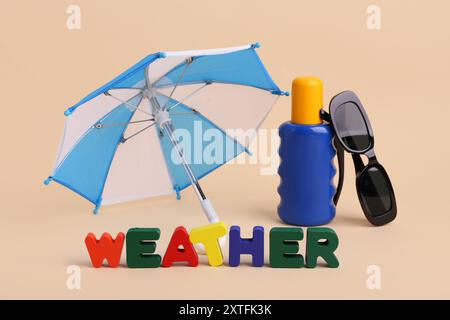 Mini umbrella with bottle of sunscreen, sunglasses and word WEATHER on beige background Stock Photo