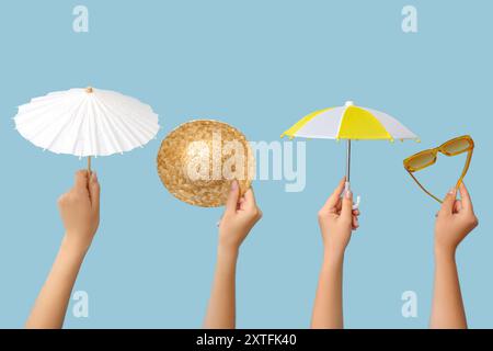 Female hands with different mini umbrellas, straw hat and sunglasses on blue background Stock Photo