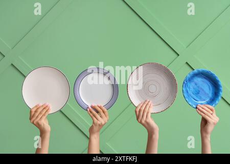 Hands holding empty plates on green background Stock Photo