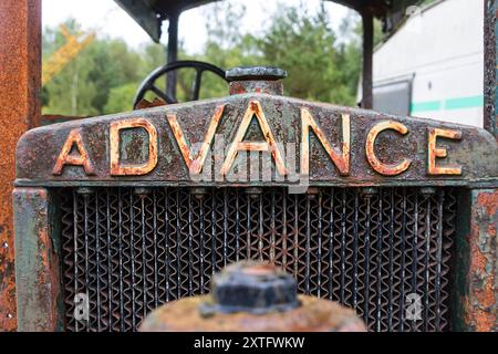 Close-up of a rusty 'Advance' sign on an antique agricultural machine or tractor, showing weathered metal and faded paint. Stock Photo