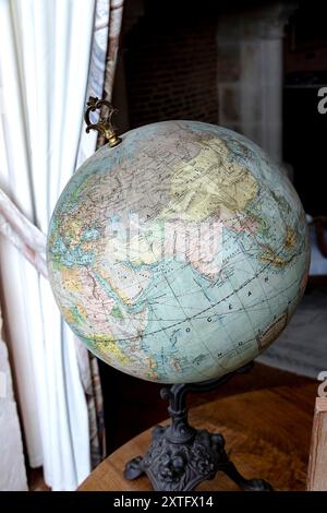 An antique globe depicting the world map positioned on a wooden surface near a window with curtains. Stock Photo