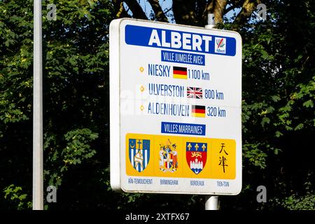 Directional sign in Albert, France, indicating sister city distances to Niesky, Ulverston, and Aldenhoven, with respective flags and logos. Stock Photo