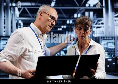 Computer scientists performing diagnostic assessments on server rigs to detect problems with data center devices. Aged specialists crosschecking checkup lists, examining for potential system defects Stock Photo