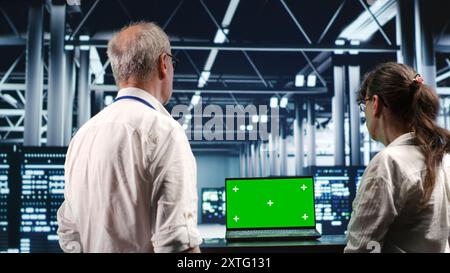 Certified IT programmers looking around high tech data center, using green screen laptop to crosscheck disaster recovery plan and assess server systems in need of replacement, preventing failures Stock Photo