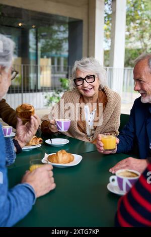 Mature grey haired woman smiling enjoying coffee with group friends on terrace of old people home. Stock Photo