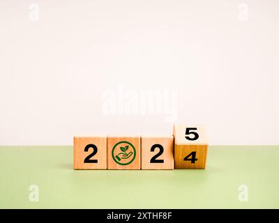 Happy new year 2025 with earth and environment care concept. Flipping wood cube block with 2024 change to 2025 calendar numbers with hand hold leaf ic Stock Photo