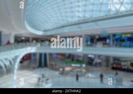 Blurred view of a shopping mall in Shenzhen, China. The image features a large open space with shops on both levels and a glass roof overhead. Stock Photo