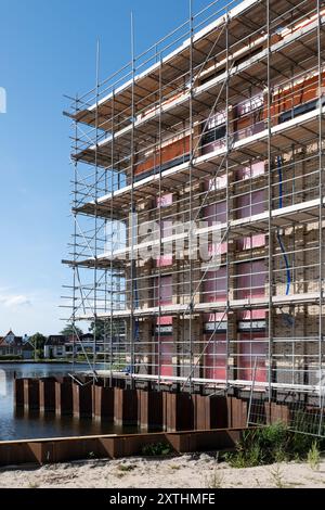 Scaffolding with platforms against a new-build apartment complex on a construction site. Metal sheet piles in water Stock Photo