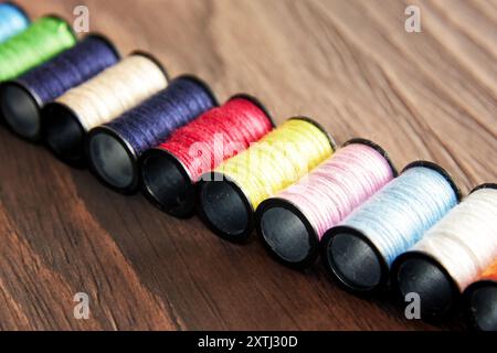 Row of colorful threads on spools are arranged on a wooden surface. Sewing equipment objects Stock Photo