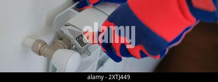 Male plumber hands in gloves installing or repairing heating radiator using wrench Stock Photo