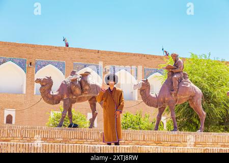 Young man in traditional Uzbek clothing at the fortress wall of the ancient city of Khiva. Khiva, Uzbekistan - July 17, 2024. Stock Photo