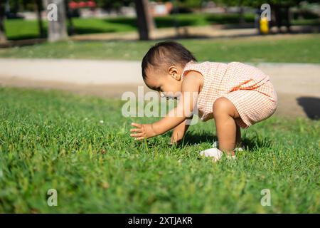 1 year old latin baby girl touching grass outdoors with copy space Stock Photo