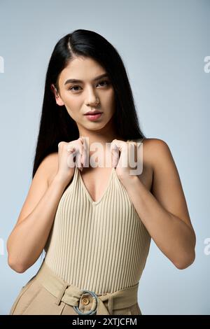 A young woman poses confidently, wearing a beige tank top and khaki pants. Stock Photo