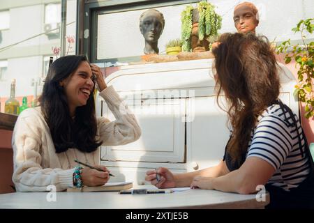Young Women friends at home writing studying and chatting among themselves are sitting with notebooks and pencils talking and studying calmly, there i Stock Photo