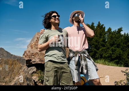 A young gay couple enjoys a summer hike in the wilderness, taking a break to sip from their mugs and admire the view. Stock Photo