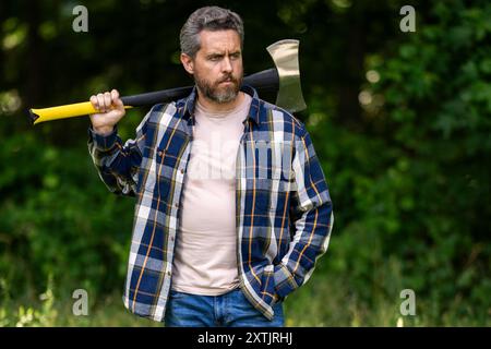 Hard working man with axe in forest. A bearded lumberjack with a large ax. Portrait of a brutal bearded man in a plaid shirt holds an axe. Male beauty Stock Photo