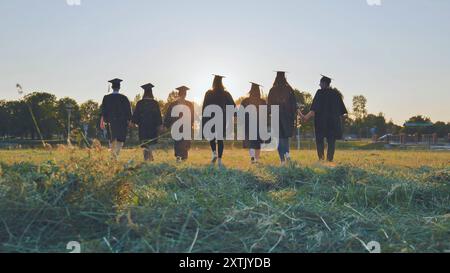 Graduate students walking through an evening meadow at sunset. Stock Photo