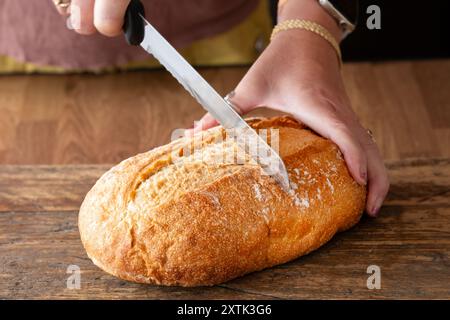 UK A loaf of freshly baked homemade traditional sourdough bread. the bread is resting on a kitchen worktop whilst being sliced by a with a bread knife Stock Photo