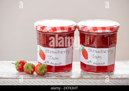 Jars of homemade Strawberry jam. The glass jars have clear handwritten labels and each jar has a cloth topping Stock Photo