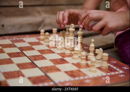 A child's hands setting up chess pieces on an outdoor chessboard, emphasizing learning, strategy, and focus in a relaxed setting. Stock Photo