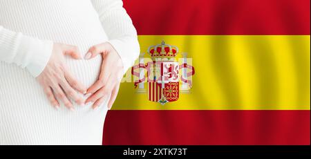 Demographics, pregnancy and love baby in Spain concept. Pregnant woman making heart against her stomach on Spanish flag background. Stock Photo