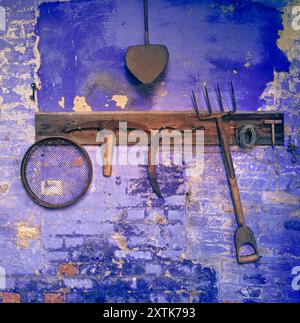 Old garden horticulture tools in brick garden bothy rustic traditional gardening tools on peeling painted blue brick wall in old garden store shed Stock Photo