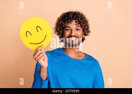Photo of cheerful happy guy wear trendy blue clothes hold yellow emoticon isolated on beige color background Stock Photo