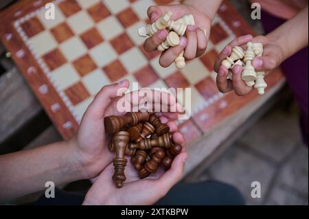 Children's hands holding chess pieces over a chessboard, representing strategic thinking and family fun during a classic board game session. Stock Photo