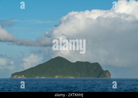 A majestic view of Guishan Island with dramatic clouds overhead. The lush green island contrasts beautifully against the blue ocean and sky. Toucheng, Stock Photo
