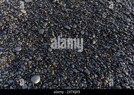 Shiny basalt pebbles on black sand, Reynisfjara Black Sand Beach, Iceland, top view, background. Stock Photo