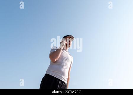 A young man in a ball cap talks on a smartphone by a lakeshore Stock Photo